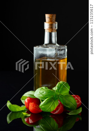 Bottle of olive oil and tomatoes with basil on a black background. 115235617