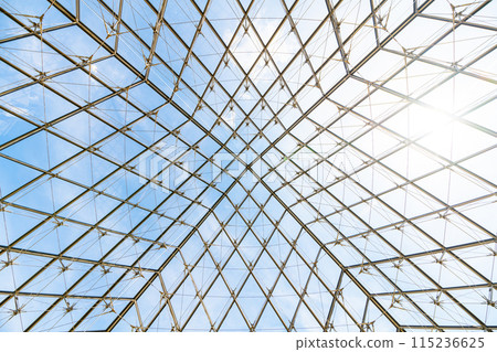 Underneath the Louvre Pyramid, the intricate glasswork contrasts against a blue sky on a clear day in Paris, France 115236625