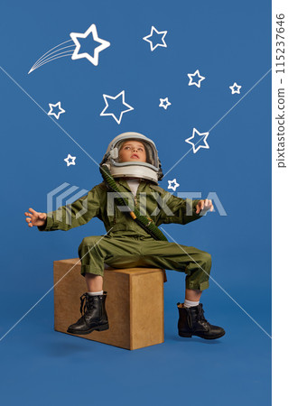 Little boy, dressed as astronaut, dreams big among hand-drawn stars surrounded cosmic elements against blue background. 115237646