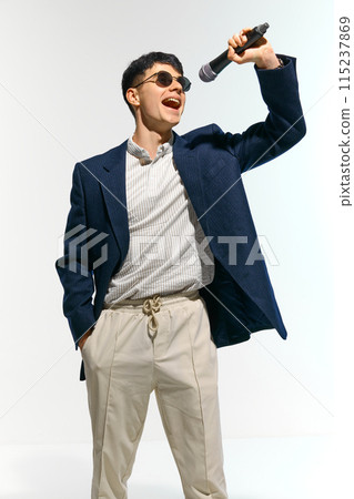 Man dressed casual attire with sunglasses performing, singing with microphone against white studio background. 115237869