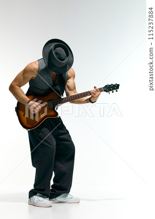 Man with white beard dressed vintage fashion outfit and hat plays electric guitar against white studio background. 115237884