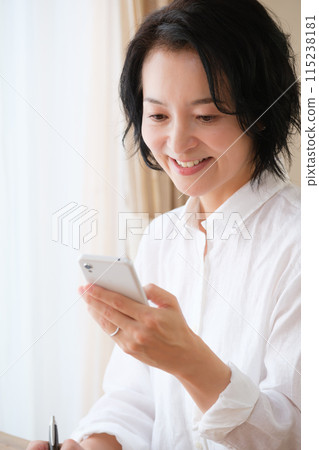 中年婦女在客廳用智慧型手機搜尋資訊並做筆記 中年婦女在客廳用智慧型手機搜尋資訊並做筆記 115238181