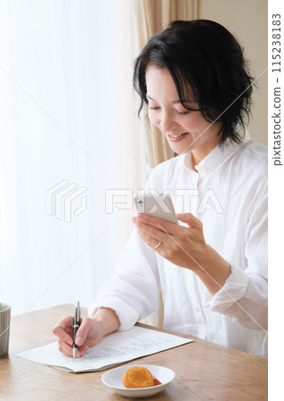 中年婦女在客廳用智慧型手機搜尋資訊並做筆記 中年婦女在客廳用智慧型手機搜尋資訊並做筆記 115238183