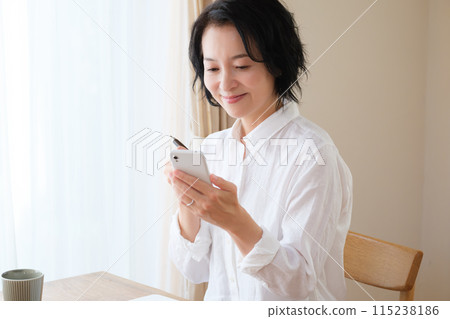 中年婦女在客廳用智慧型手機搜尋資訊並做筆記 中年婦女在客廳用智慧型手機搜尋資訊並做筆記 115238186