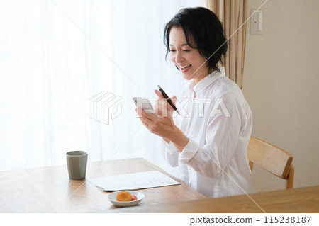 中年婦女在客廳用智慧型手機搜尋資訊並做筆記 115238187