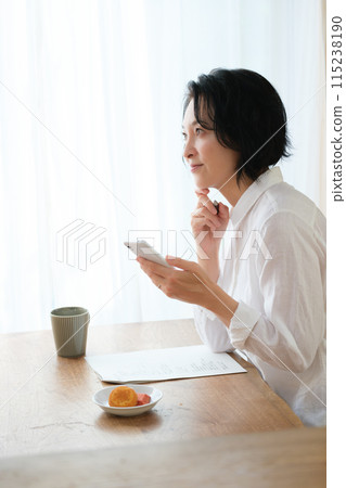 中年婦女在客廳用智慧型手機搜尋資訊並做筆記 115238190