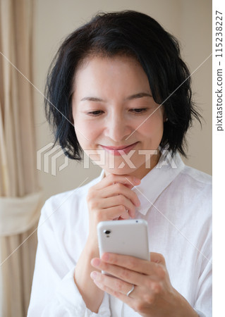 中年婦女在客廳用智慧型手機搜尋資訊並做筆記 中年婦女在客廳用智慧型手機搜尋資訊並做筆記 115238227