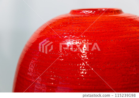 An empty round red vase stands in front of white wall, close up 115239198