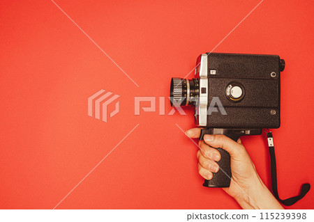vintage portable movie camera in a woman's hand on a red background. retro, 70s, 80s vintage portable movie camera in a woman's hand on a red background. retro, 70s, 80s 115239398