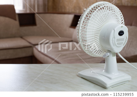 White plastic fan back view with the mode turned on for cool air in room, increasing the temperature of house on hot day using an electronic fan White plastic fan back view with the mode turned on for cool air in room, increasing the temperature of house on hot day using an electronic fan 115239955