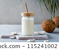 A jar of fresh coconut milk with a bamboo straw on a wooden cutting board, surrounded by coconut pieces and whole coconuts. 115241002