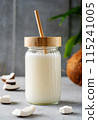 A jar of fresh coconut milk with a bamboo straw, surrounded by coconut pieces and a whole coconut on a textured surface. 115241005