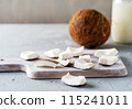 Freshly sliced coconut pieces arranged on a wooden cutting board with a whole coconut and a jar of coconut milk in the background. 115241011