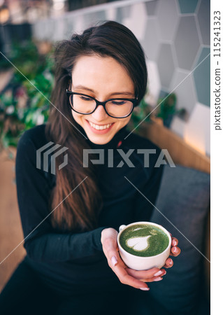 Adorable young woman drinking matcha tea in cozy cafe 115241323