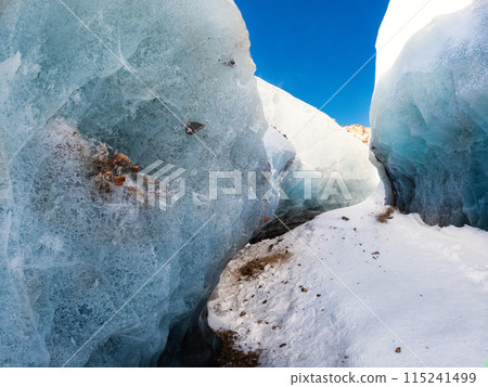 Amazing winter landscape on the way to a mountain glacier, a path surrounded by a blue transparent ice corridor interspersed with mountain stones. Amazing winter landscape on the way to a mountain glacier, a path surrounded by a blue transparent ice corridor interspersed with mountain stones. 115241499