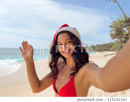 Woman in Santa Hat Waving on Sunny Tropical Beach Woman in Santa Hat Waving on Sunny Tropical Beach 115242161