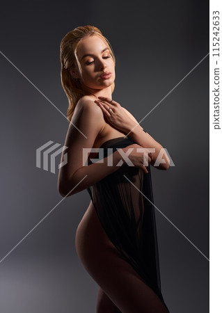 Sensual naked woman covering body with fabric in dark studio 115242633