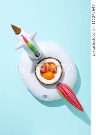 Inflatable ring for swimming and kumquat in half coconut on blue background, top view Inflatable ring for swimming and kumquat in half coconut on blue background, top view 115242647