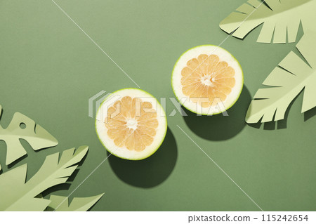Two half of pomelo fruit and paper tropical leaves on green background, top view Two half of pomelo fruit and paper tropical leaves on green background, top view 115242654