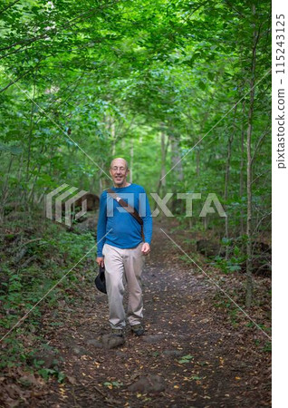 Active senior man hiking on a woodland trail green foliage Active senior man hiking on a woodland trail green foliage 115243125