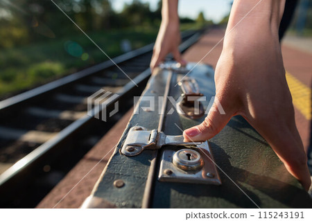 A girl fastens the zipper on an old travel suitcase on a train platform one summer afternoon during a planned train trip. A girl fastens the zipper on an old travel suitcase on a train platform one summer afternoon during a planned train trip. 115243191