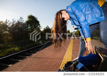 Teenagers spilled the contents of a travel suitcase on the train platform. An unfastened travel suitcase. Adventure on the platform. Teenagers spilled the contents of a travel suitcase on the train platform. An unfastened travel suitcase. Adventure on the platform. 115243201