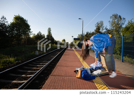 Teenagers spilled the contents of a travel suitcase on the train platform. An unfastened travel suitcase. Adventure on the platform. Teenagers spilled the contents of a travel suitcase on the train platform. An unfastened travel suitcase. Adventure on the platform. 115243204