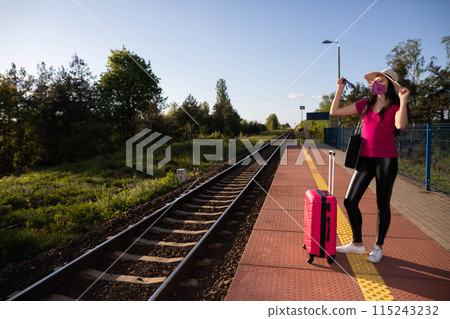 A teenage girl is standing in a face mask on a train platform waiting for her train. A summer adventure in rail travel. 115243232