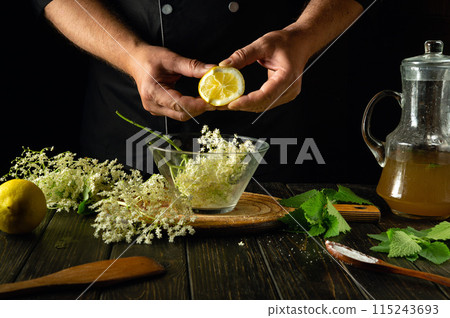 Cooking healthy kvass from elderflowers and lemon on the kitchen table by the hands of a cook. Refreshing and healing drink with mint and elderberry 115243693