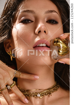Beautiful tanned woman with smoky makeup, gold jewelry and ice. Beauty face. Beautiful tanned woman with smoky makeup, gold jewelry and ice. Beauty face. 115244260