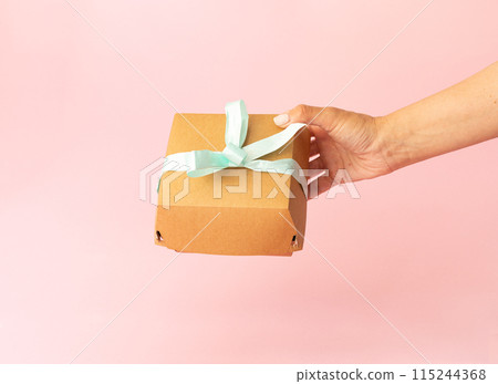 cardboard packaging in female hand, bento cake on light pink background, light blue bow 115244368