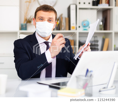 Man in protective face mask working at office 115244390