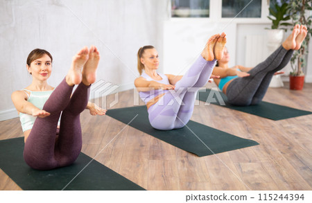 Sporty woman sitting in boat pose during group yoga workout 115244394