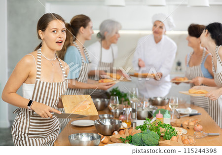 Girl at group class of culinary school cuts up chicken and prepares low-calorie diet lunch 115244398