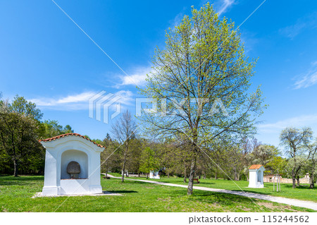 Small chapels at Skalka Calvary stand amidst vibrant green trees under a clear blue sky, signaling the arrival of spring. Mnisek pod Brdy, Czechia Small chapels at Skalka Calvary stand amidst vibrant green trees under a clear blue sky, signaling the arrival of spring. Mnisek pod Brdy, Czechia 115244562
