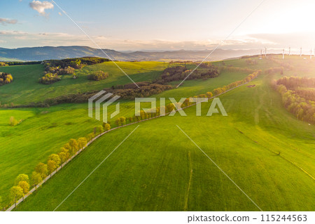 Dawn breaks over a lush spring landscape, with a series of wind turbines standing along the horizon, symbolizing a harmony between technology and nature. Dawn breaks over a lush spring landscape, with a series of wind turbines standing along the horizon, symbolizing a harmony between technology and nature. 115244563