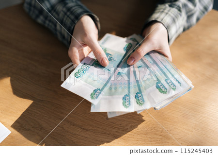 High-angle view of unrecognizable female counting stack of Russian rubles banknotes. Closeup of businesswoman counting cash sitting at office desk. Concept of investment, money exchange, bribes. 115245403