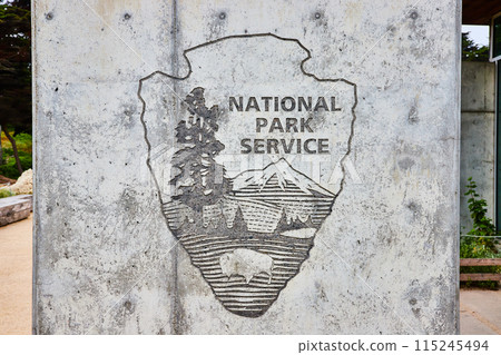 Embedded National Park Service logo on textured concrete wall framed by Lands End Lookout park Embedded National Park Service logo on textured concrete wall framed by Lands End Lookout park 115245494