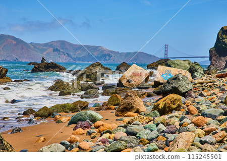 Distant Golden Gate Bridge with close view of colorful pebble strewn shore with graffiti structure 115245501
