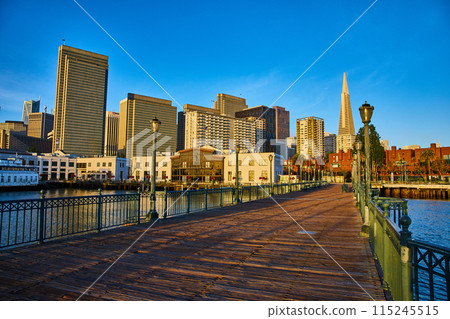 Dark wood Pier 7 with golden light striking skyscrapers at sunrise with bright blue sky 115245515