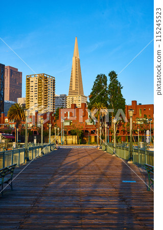 Dark wood pier with sunrise striking Transamerica Pyramid and other buildings 115245523