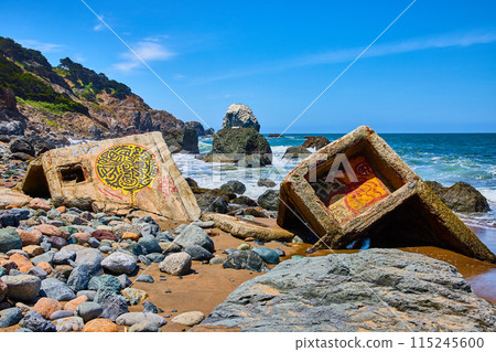 Colorful rocks around graffiti covered concrete fragments washed ashore from ocean Colorful rocks around graffiti covered concrete fragments washed ashore from ocean 115245600