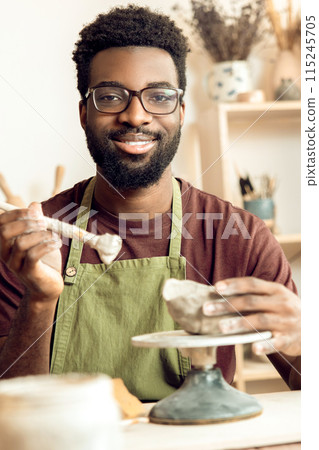 Dark-skinned bearded painting pottery and looking contented 115245705