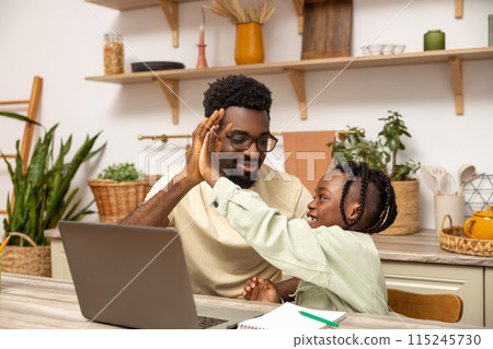 Black father with daughter doing online tasks on laptop 115245730