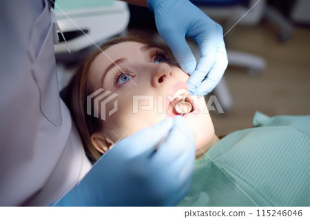 Dentist and patient at modern medical center. Doctor treats a young woman teeth in hospital. Practitioner examines the patient before orthodontists or prosthetics treatment. 115246046