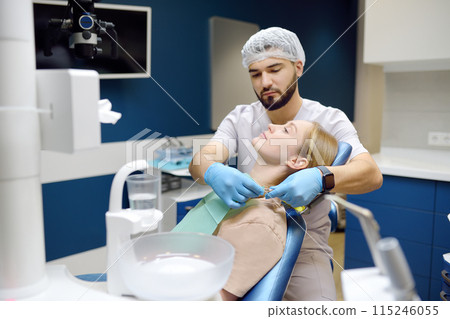 Doctor prepares young woman for teeth treatment in hospital. Practitioner dentist examines the patient before orthodontists or prosthetics treatment in modern medical center. Doctor prepares young woman for teeth treatment in hospital. Practitioner dentist examines the patient before orthodontists or prosthetics treatment in modern medical center. 115246055