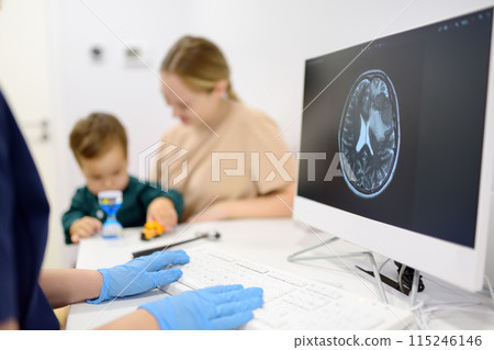 Toddler boy with his mom are at appointment with a pediatric neurologist. A doctor exploring of baby x-ray scan image brain on computer monitor. 115246146
