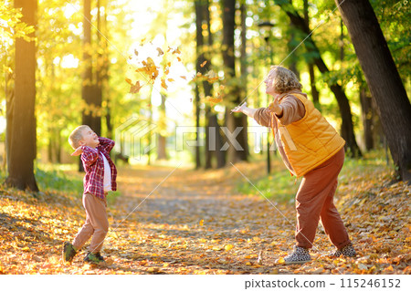Mother and her son are having fun in the autumn park. A beautiful woman throws up yellow maple leaves while her adorable toddler child spins. Mother and her son are having fun in the autumn park. A beautiful woman throws up yellow maple leaves while her adorable toddler child spins. 115246152