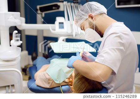 Dentist and patient at modern medical center. Doctor treats a young woman teeth in hospital. Practitioner examines the patient before orthodontists or prosthetics treatment. Dentist and patient at modern medical center. Doctor treats a young woman teeth in hospital. Practitioner examines the patient before orthodontists or prosthetics treatment. 115246289