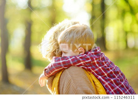 Close-up portrait of a mother and son during a walk in the autumn park. Woman holds her toddler son in her arms and hugs him tenderly. 115246311